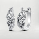 A pair of polished silver huggie hoop earrings featuring detailed wing designs, displayed on a clean light gray background.