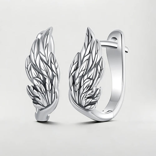 A pair of polished silver huggie hoop earrings featuring detailed wing designs, displayed on a clean light gray background.