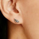 A close-up of a person's ear wearing a small silver wing stud earring.