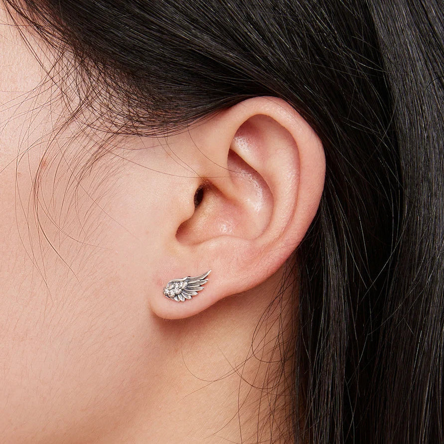 A close-up of a person's ear wearing a small silver wing-shaped stud earring.